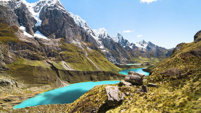A scenic view of a mountain range with snow-capped peaks and a turquoise lake in the foreground in Peru - Outer